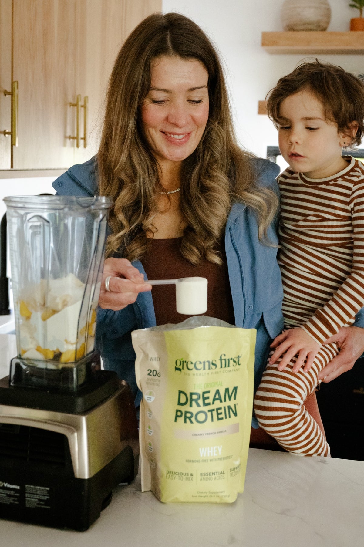 Dream Protein Whey Lifestyle Group - Woman holding a scoop beside a child and a fruit-filled blender